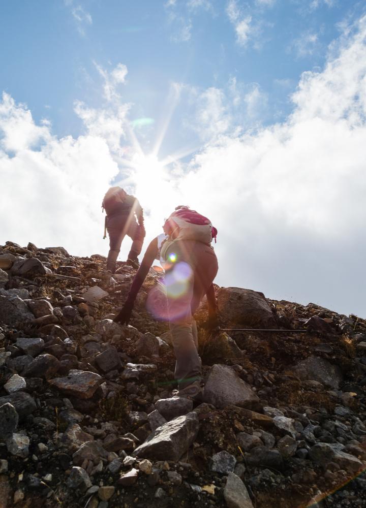 Looking up at two people scrambling up some rocks
