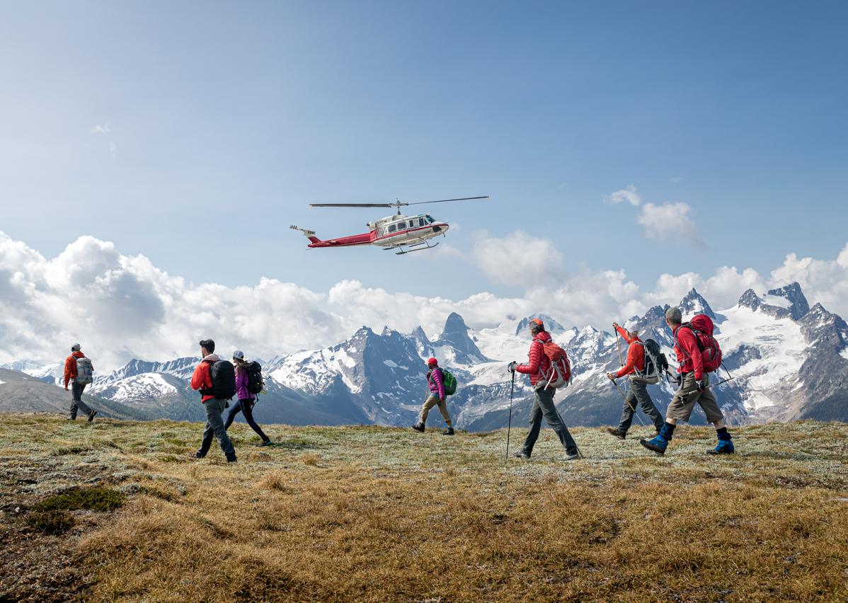 A group of people walking underneath a helicopter with a mountain range in the background
