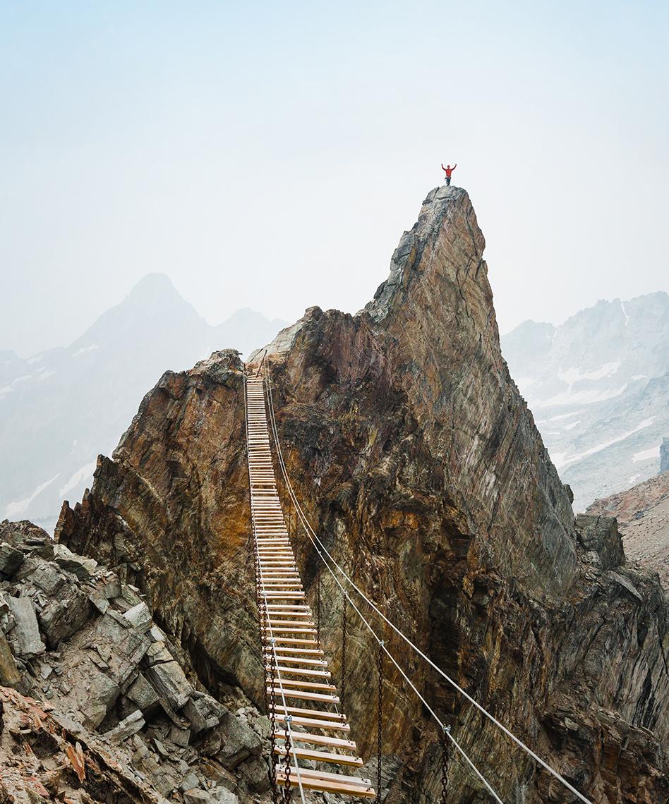 image of a hanging wooden bridge over to another peak with a person at the top
