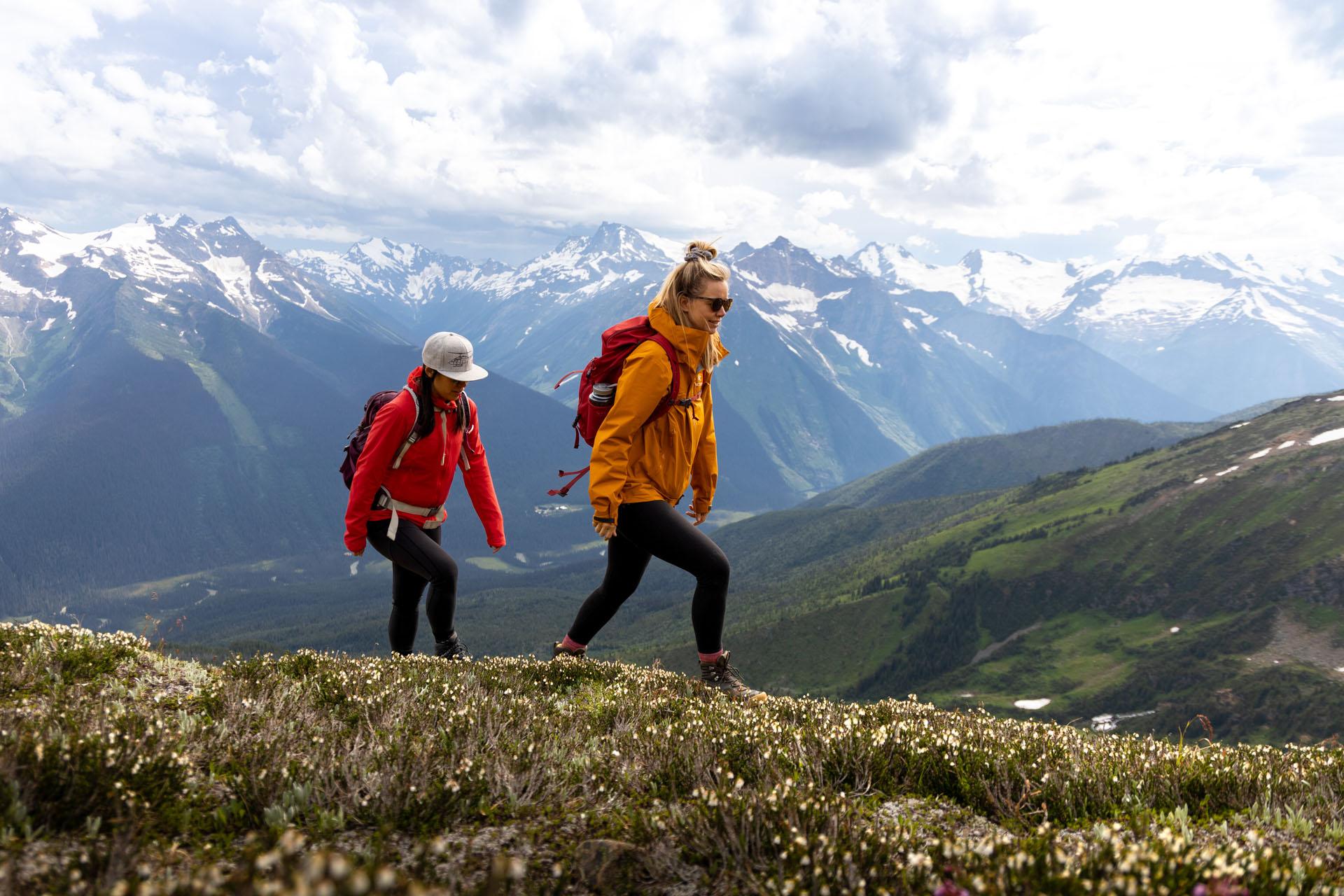 two hikers wearing red and orange coats make their way through the alpine