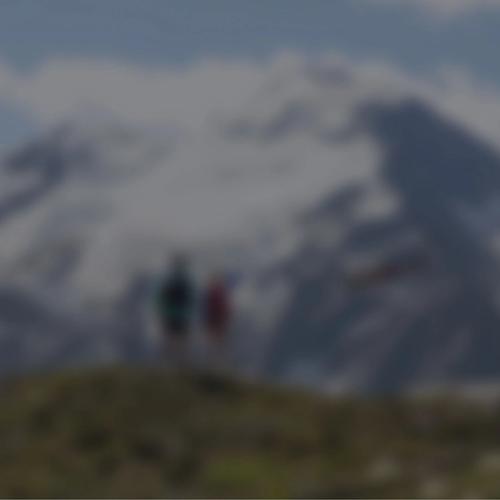 Two people watching a helicopter go by in a valley of mountains