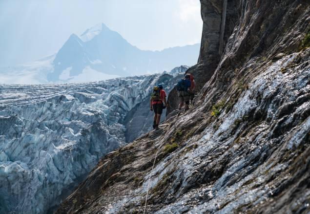 People climbing on a steep ridge with a glacier in the background