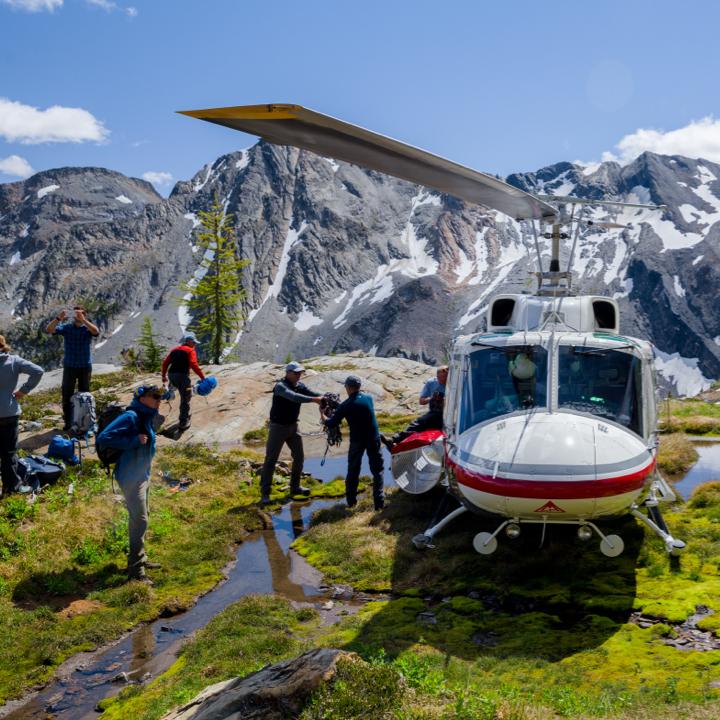 a group of people getting off a helicopter with mountains in the background