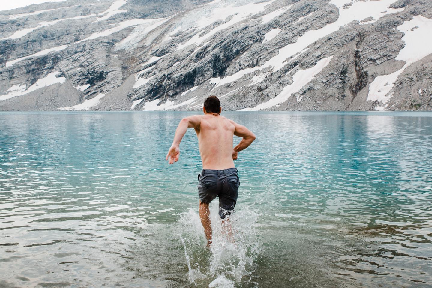 A man running into a glacial lake in shorts