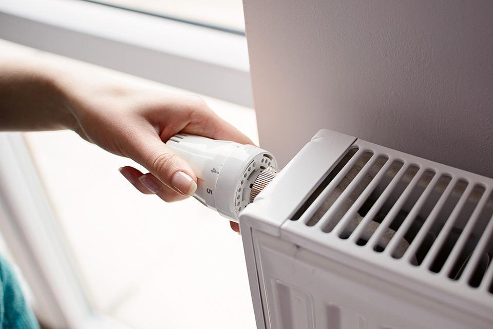 En hand vrider ner termostaten på ett element