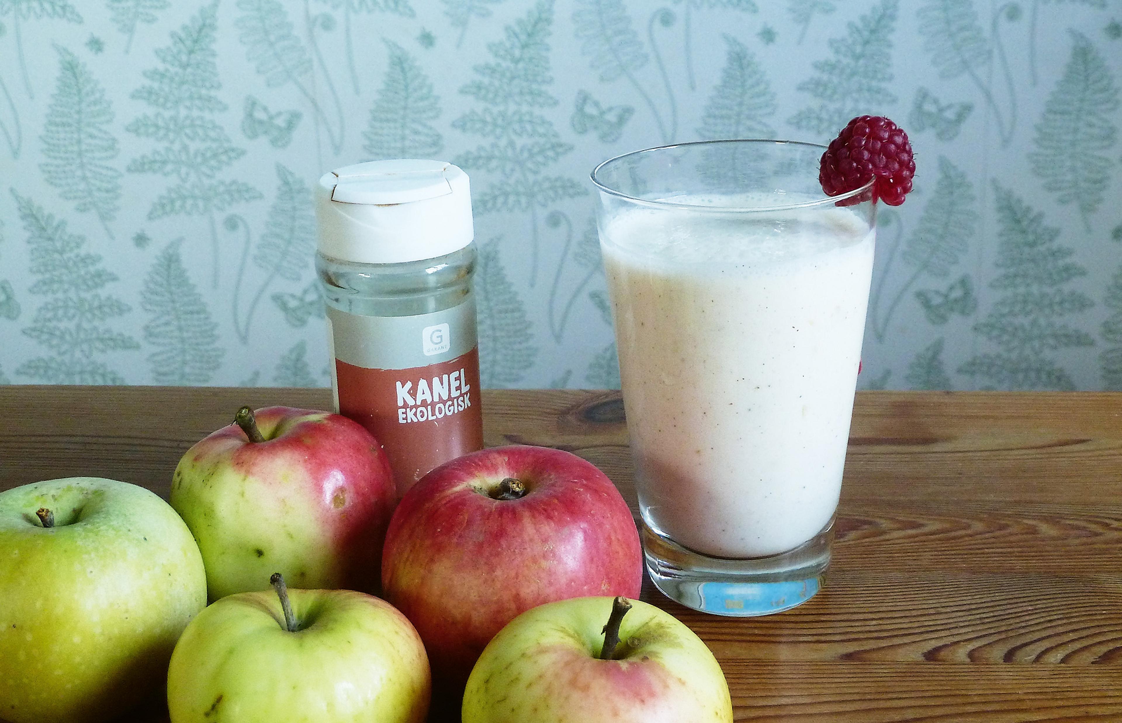 Äppelsmoothie i ett glas bredvid äpplen och en burk kanel