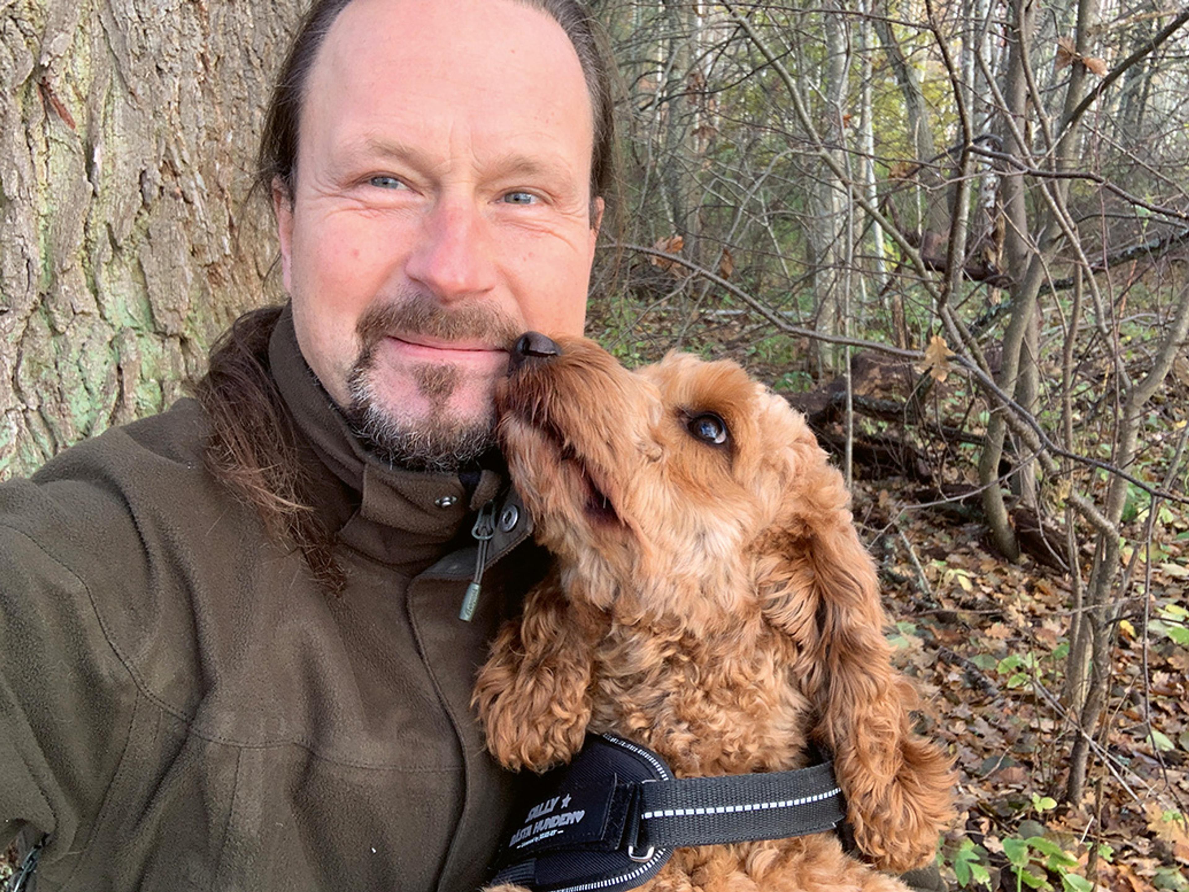 Fredrik Nyström i skogen med en hund som slickar honom på kinden