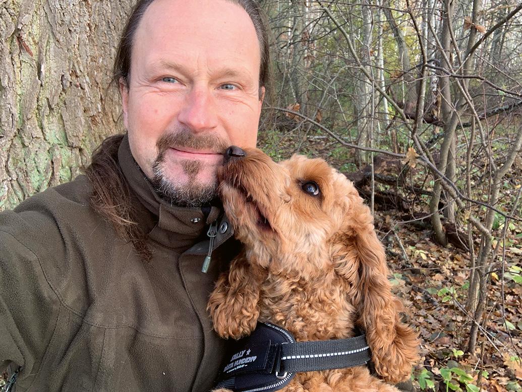 Fredrik Nyström i skogen med en hund som slickar honom på kinden