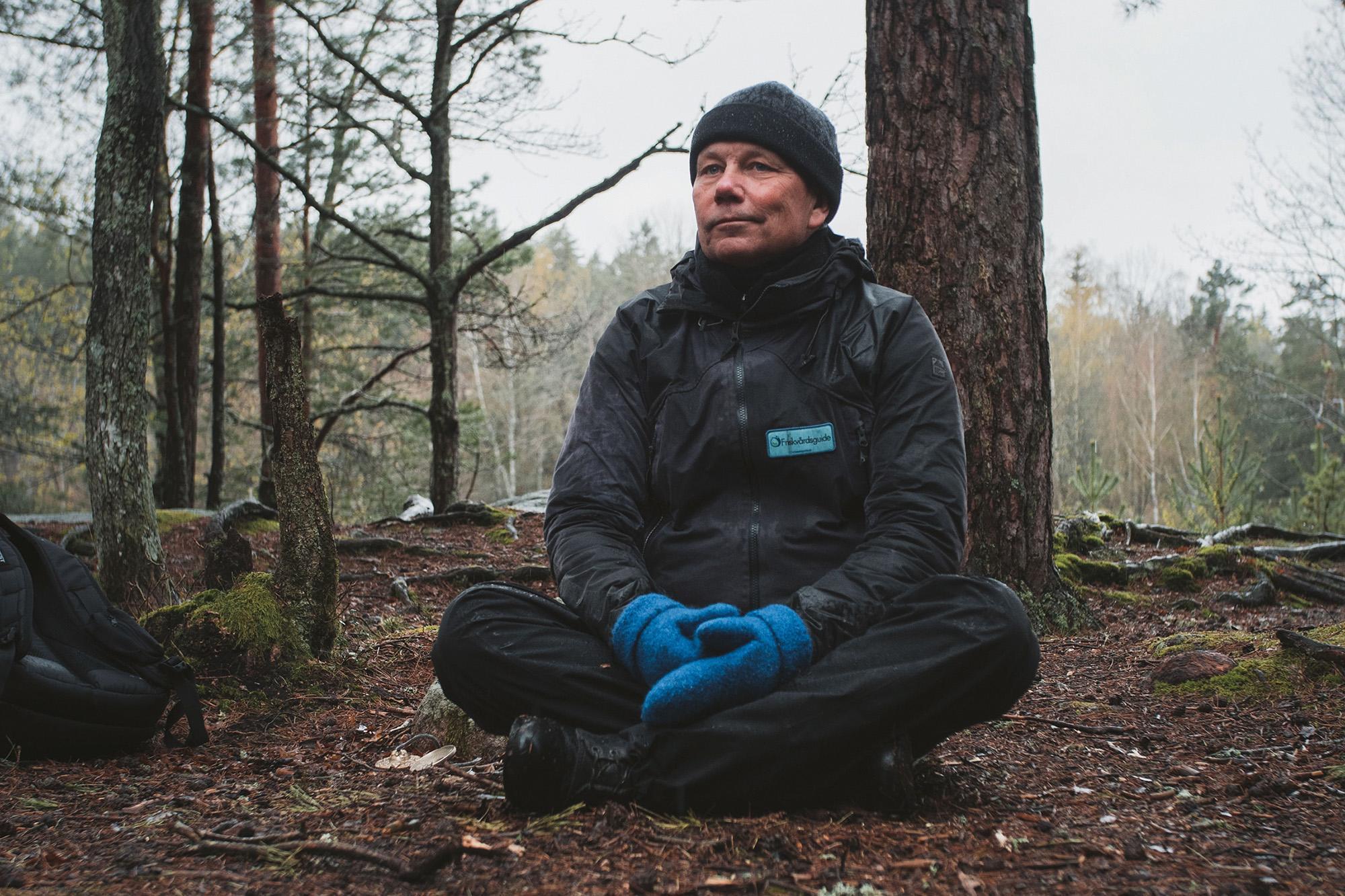 Bosse Rosén sitter stilla i skräddarställning på marken i en skog