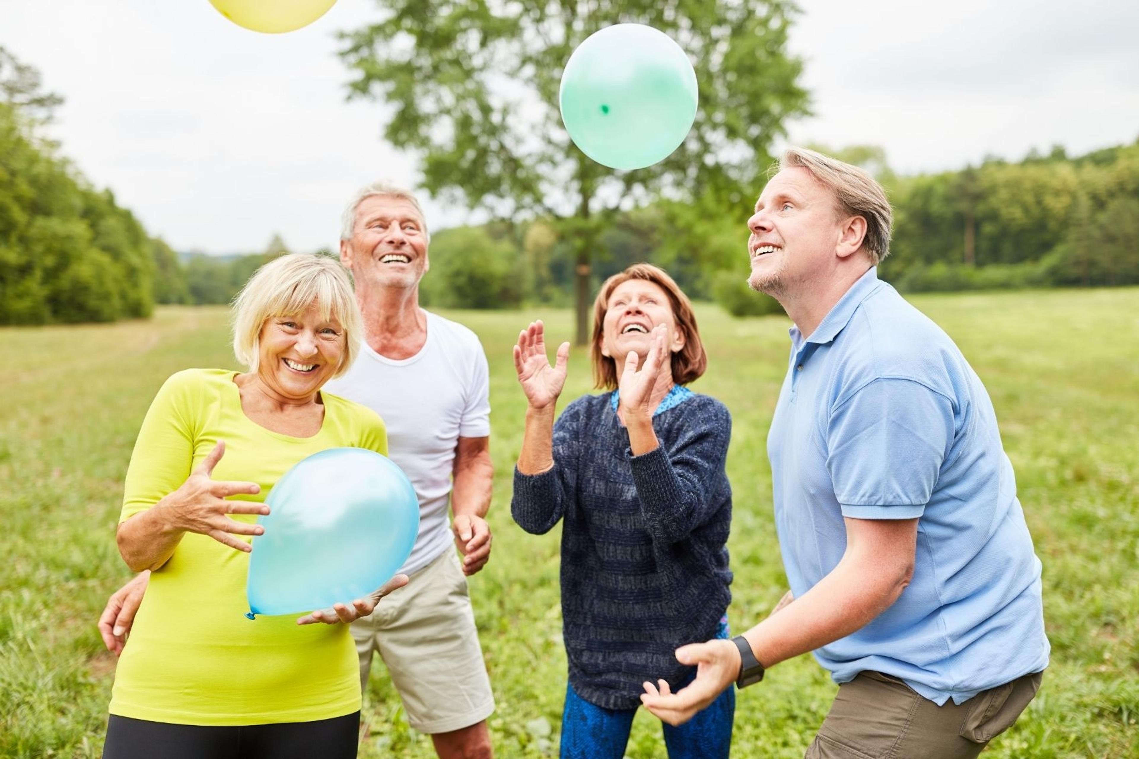 Fyra glada seniorer leker med ballonger på en äng