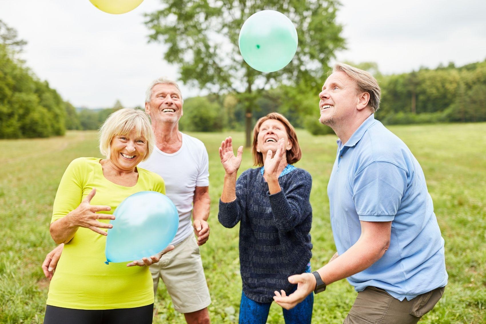 Fyra glada seniorer leker med ballonger på en äng