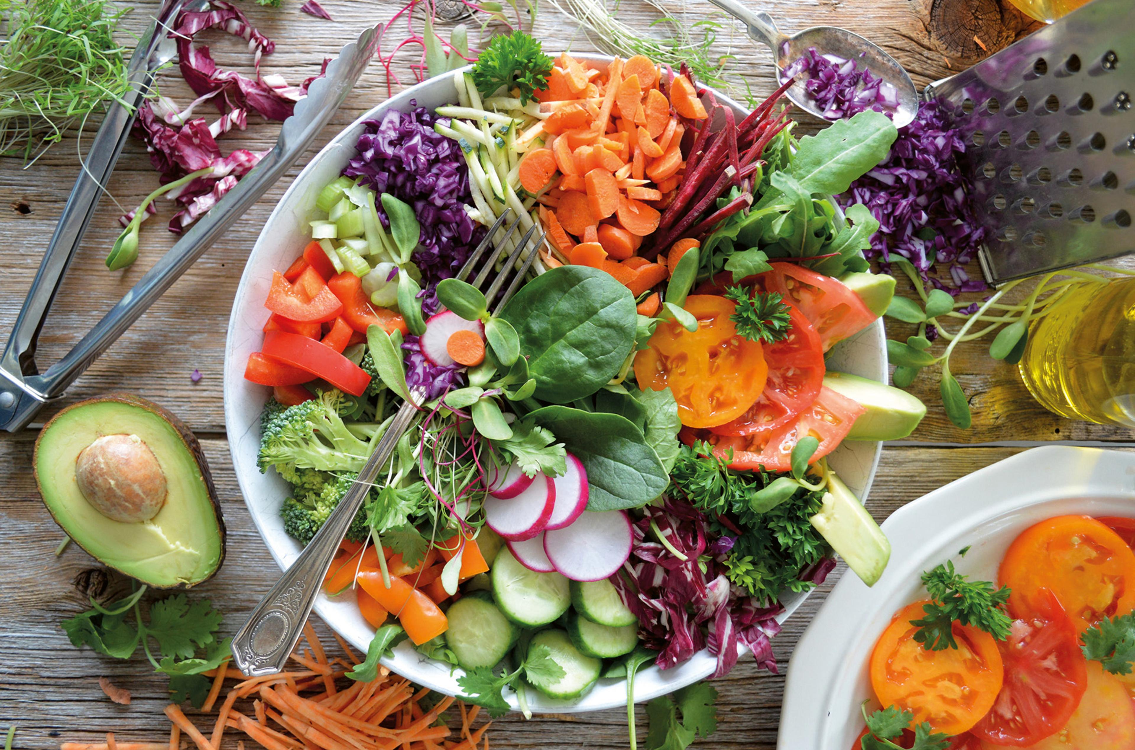 Stor skål med färgglad sallad av råa grönsaker, bredvid en halverad avokado