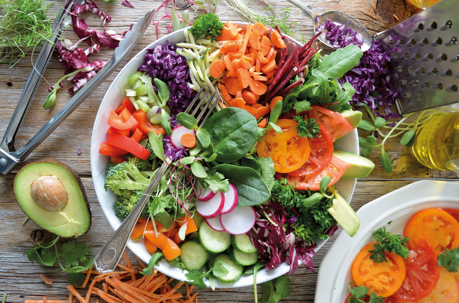 Stor skål med färgglad sallad av råa grönsaker, bredvid en halverad avokado