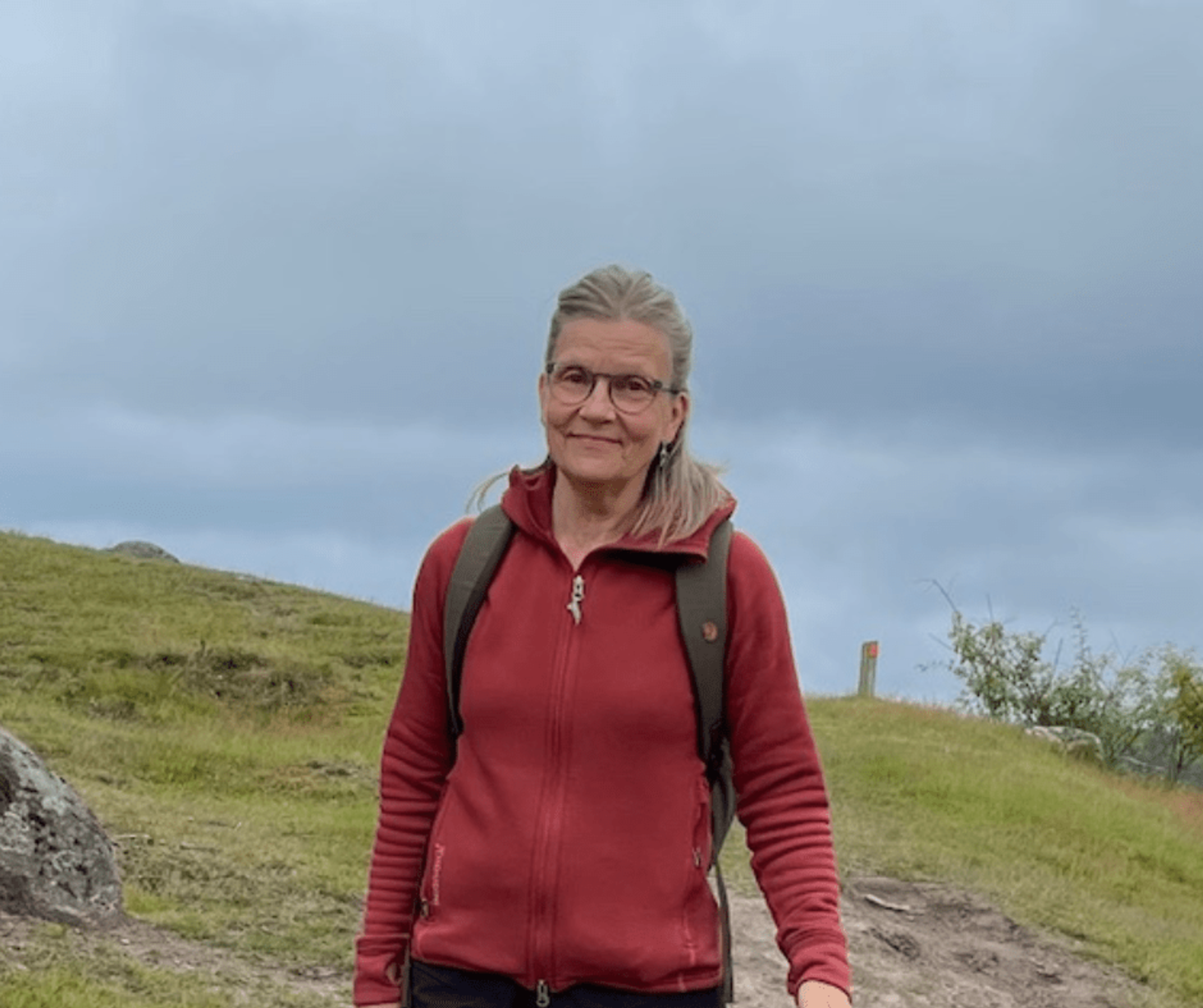 Porträtt av Karin Lilje i röd jacka ute på en grön kulle