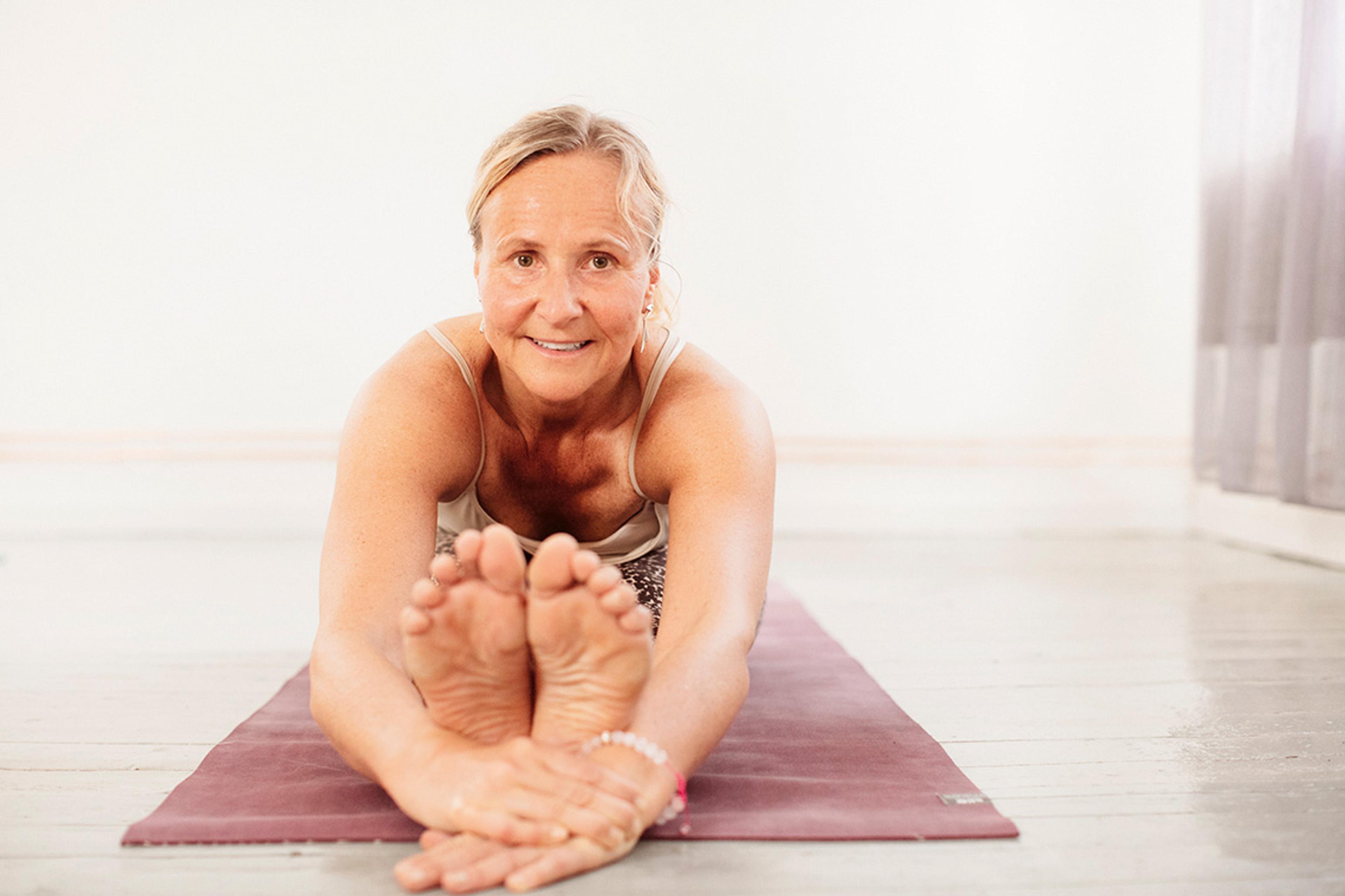 Ann Svärdfelt sitter på en yogamatta och sträcker sig fram mot fötterna