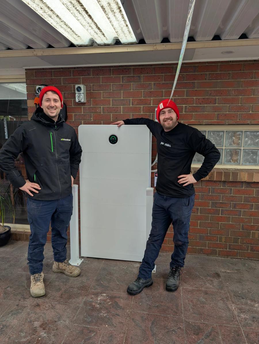 Two Revelectrical electricians beside a home battery they have just installed