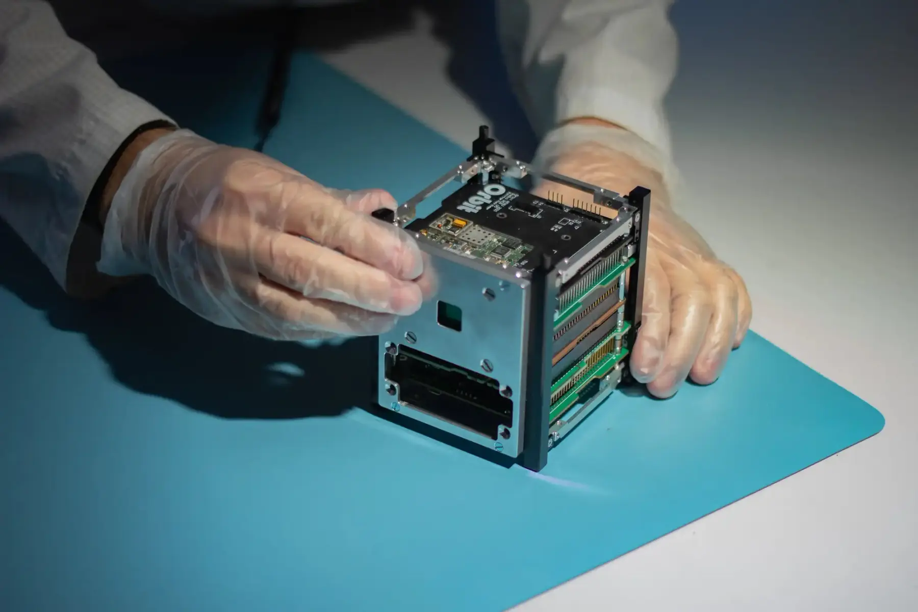 Cubesat being handled by a person with plastic gloves and labcoat.
