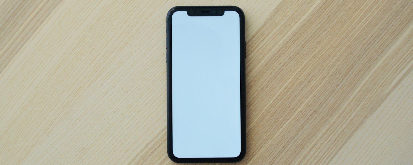 A black smartphone with a blank white screen on a light wooden surface