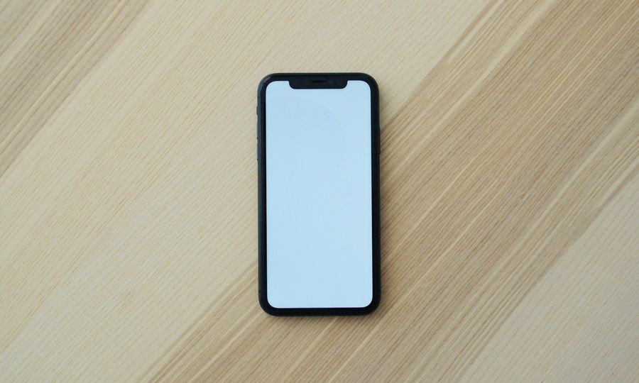 A black smartphone with a blank white screen on a light wooden surface