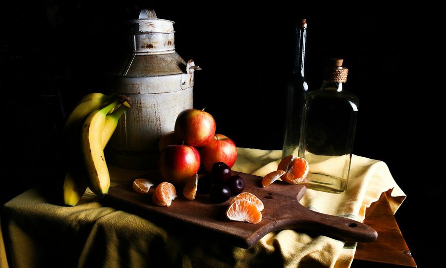 A wooden cutting board topped with fruit next to a bottle of wine