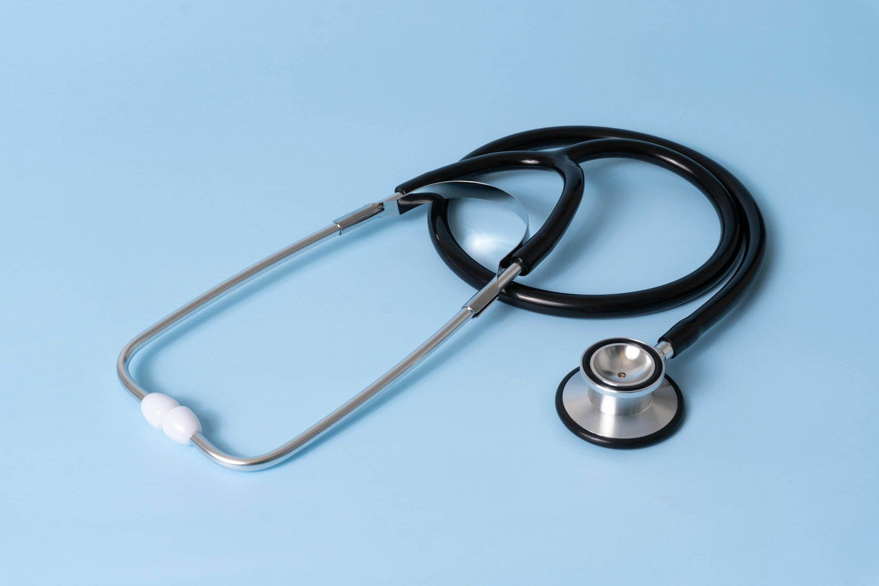 A black medical stethoscope with silver chest piece on a light blue background
