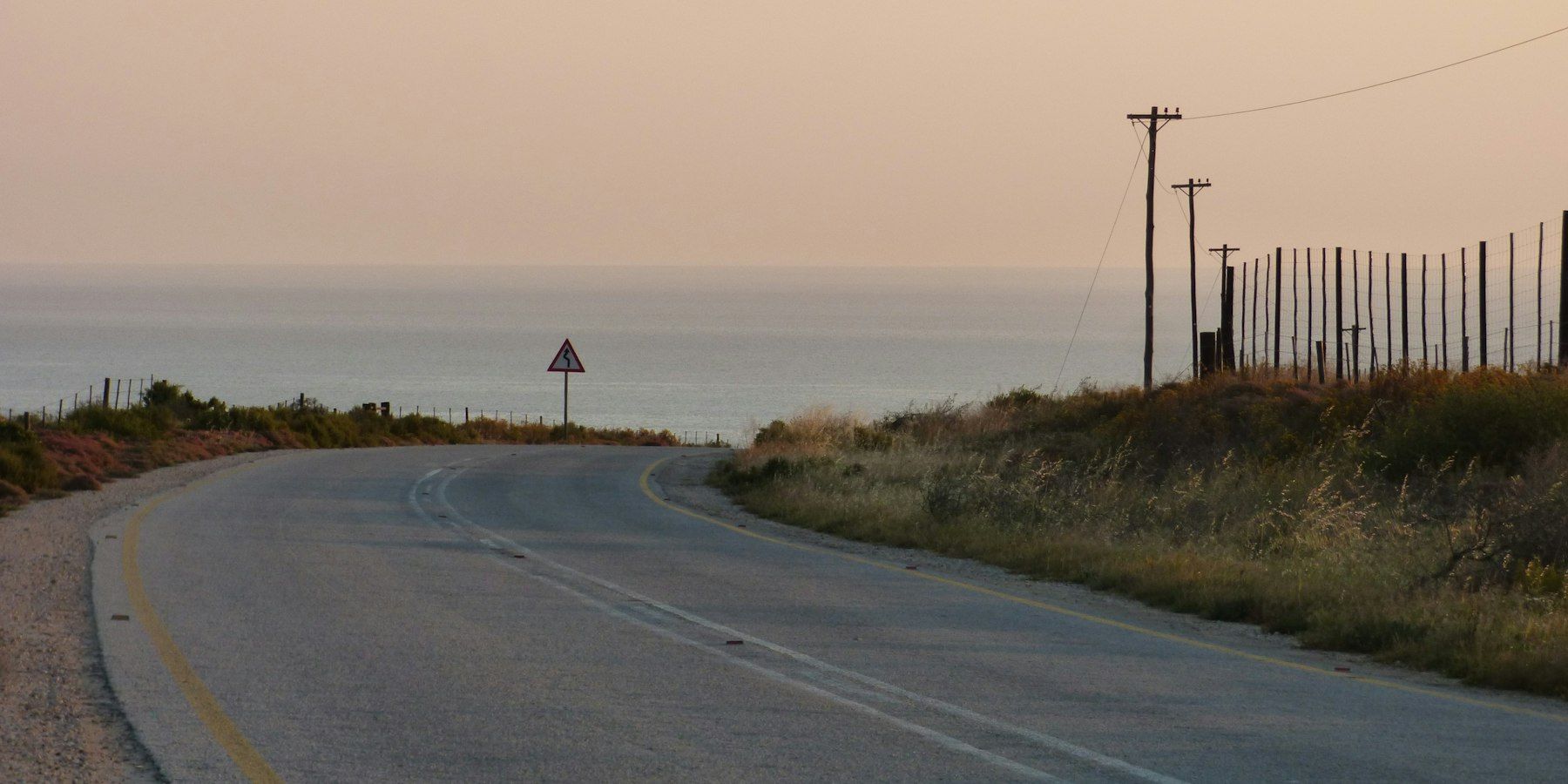 A winding road leading toward the ocean under a soft warm sky