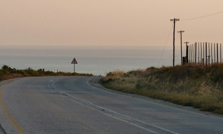 A winding road leading toward the ocean under a soft warm sky
