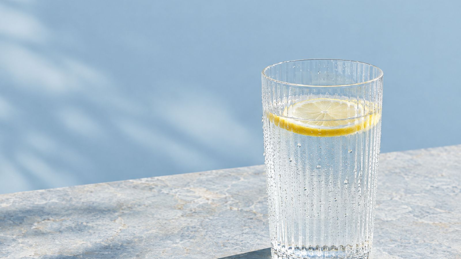 A glass of water with a slice of lemon in the sunlight