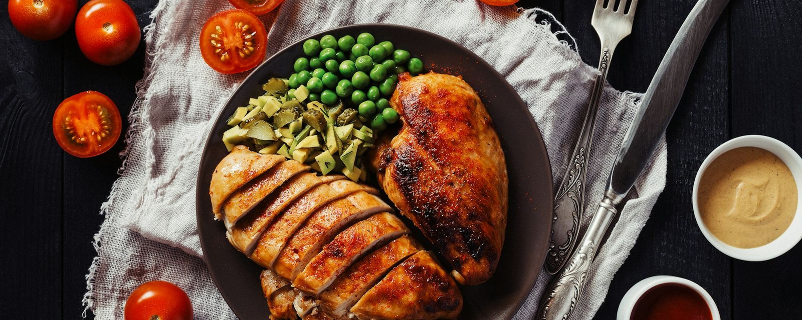 Sliced chicken breast with green peas and chopped pickles on a dark plate