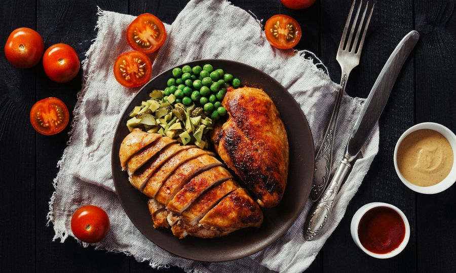 Sliced chicken breast with green peas and chopped pickles on a dark plate