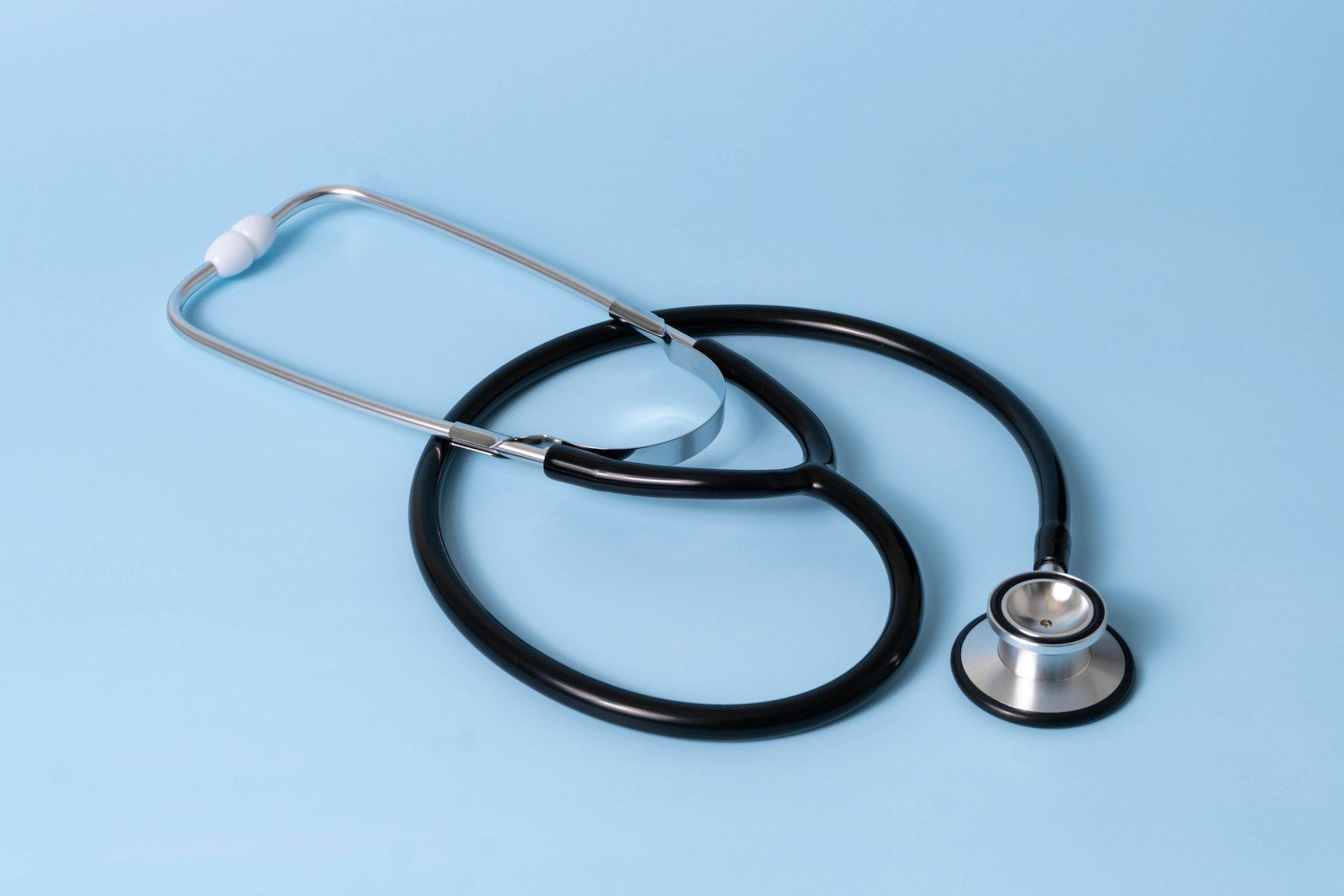 A black medical stethoscope with silver chest piece on a light blue background