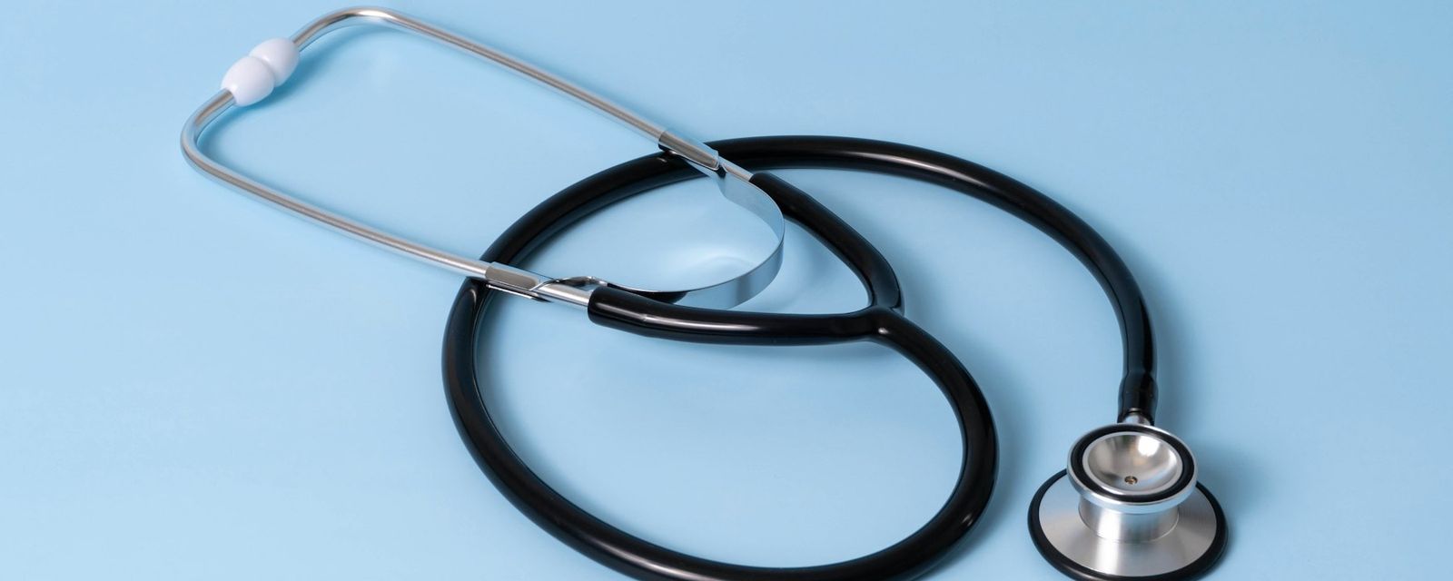 A black medical stethoscope with silver chest piece on a light blue background