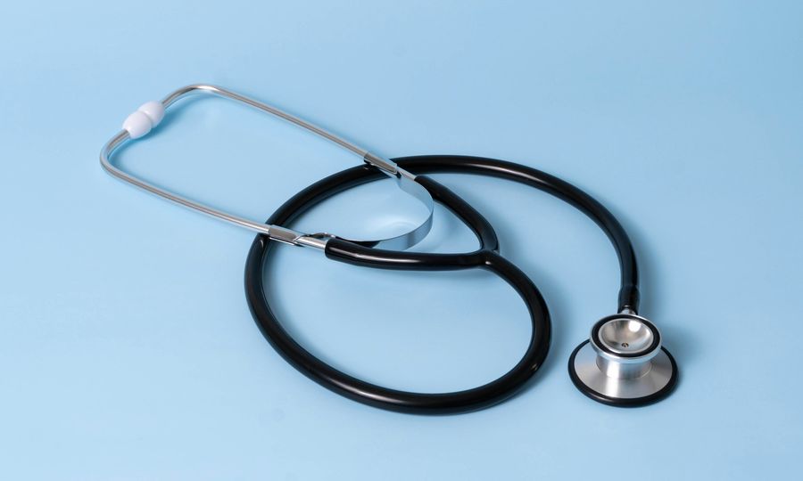A black medical stethoscope with silver chest piece on a light blue background