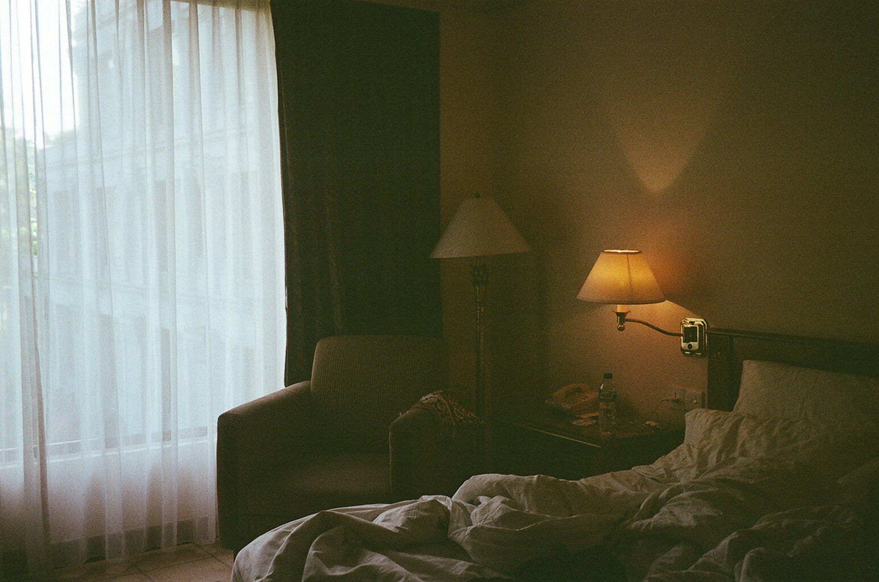 A bedroom with a bed, chair, lamp and window