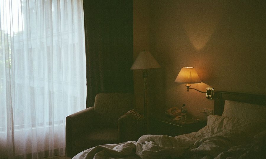 A bedroom with a bed, chair, lamp and window