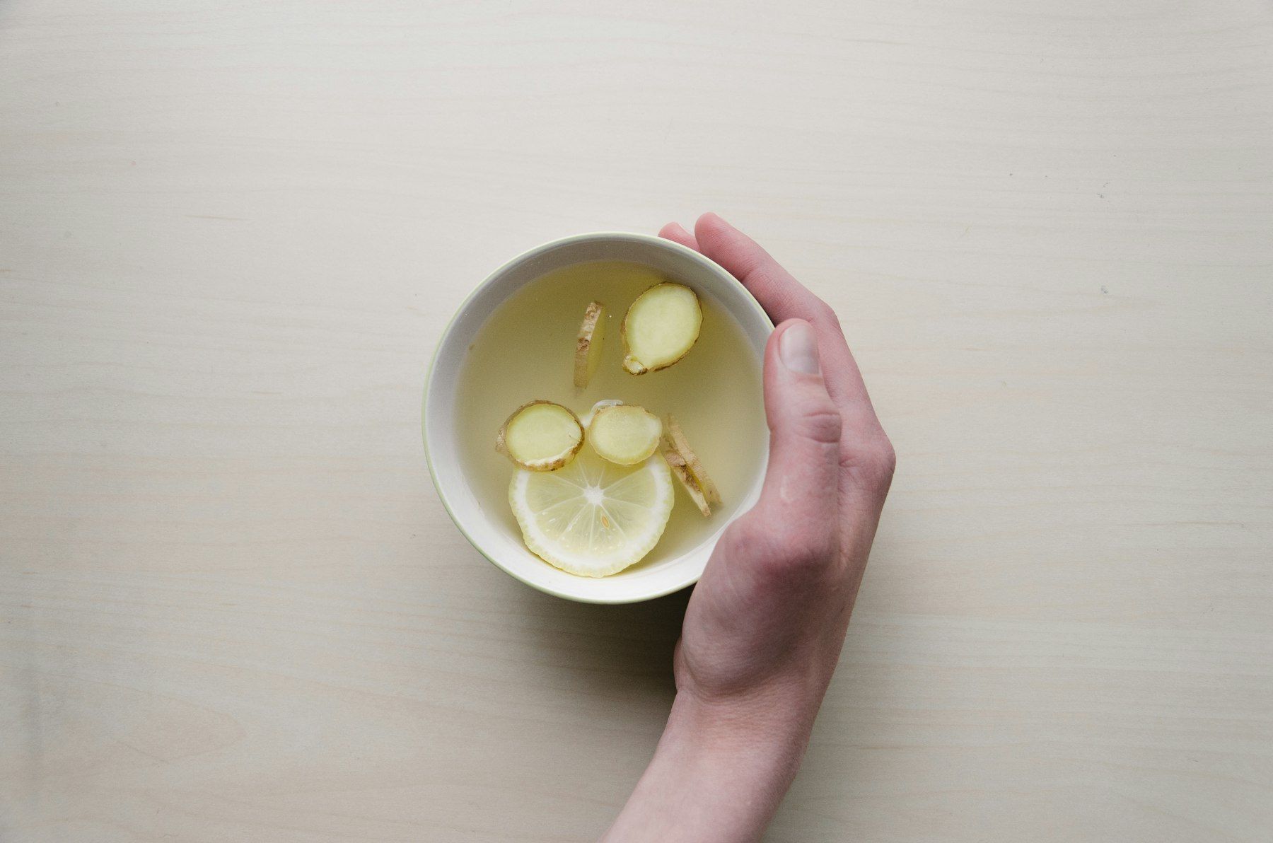 Person holding white bowl with sliced lime and ginger inside