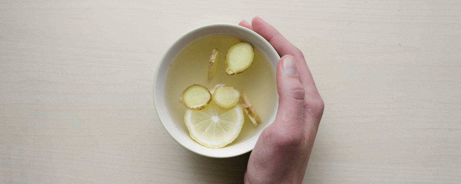 Person holding white bowl with sliced lime and ginger inside