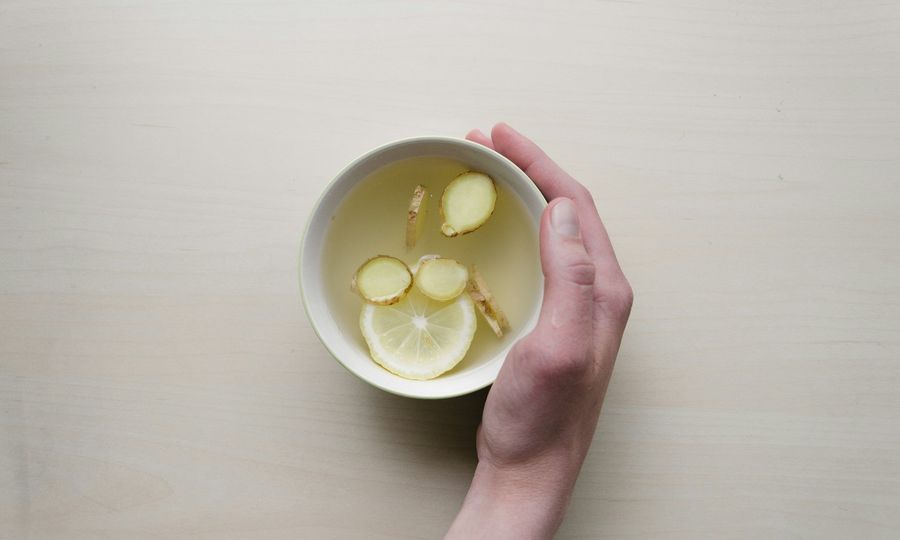 Person holding white bowl with sliced lime and ginger inside