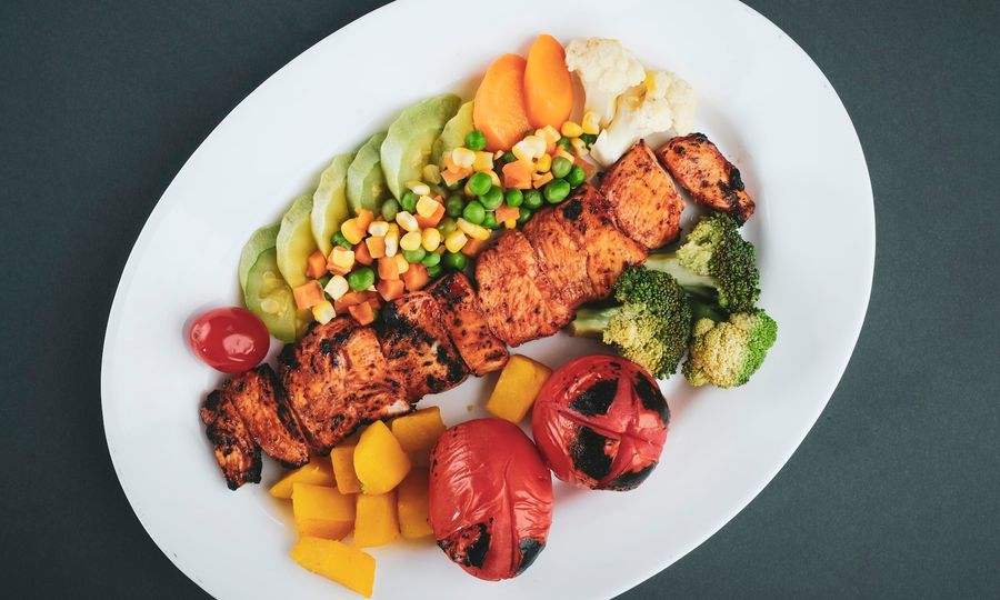 Grilled meat with sliced lemon and sliced tomatoes on white ceramic plate