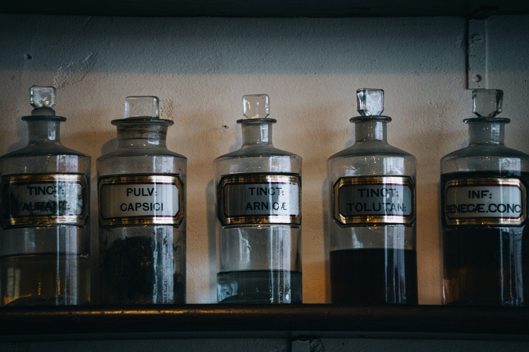 Five vintage apothecary bottles with labels on shelf