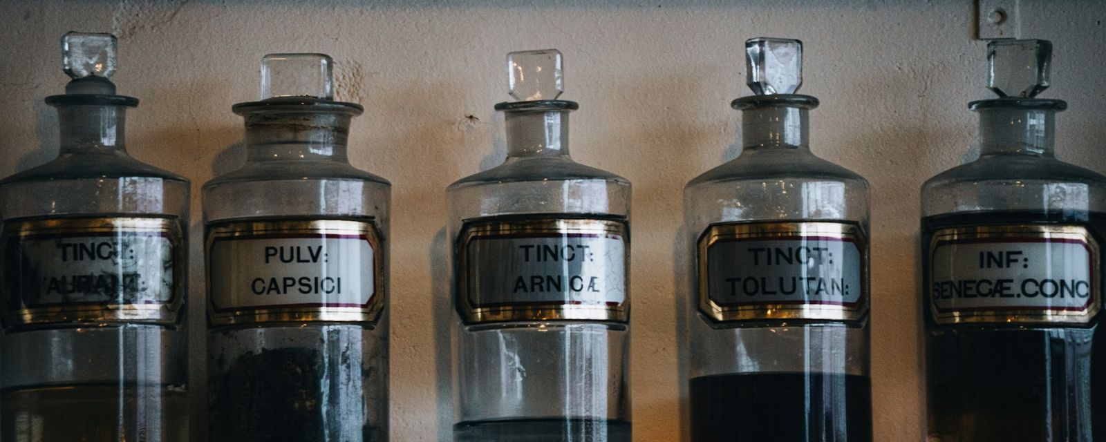 Five vintage apothecary bottles with labels on shelf