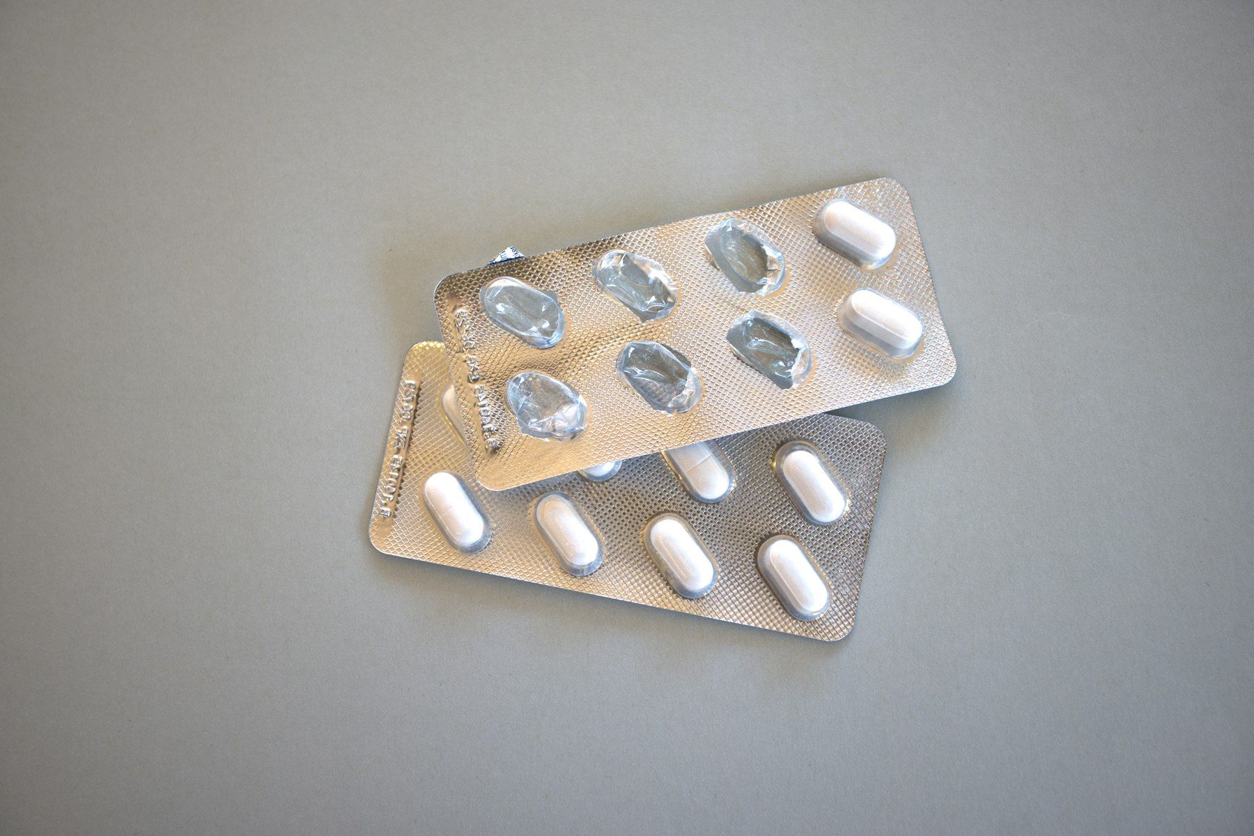 Two silver blister packs with white pills on a grey surface