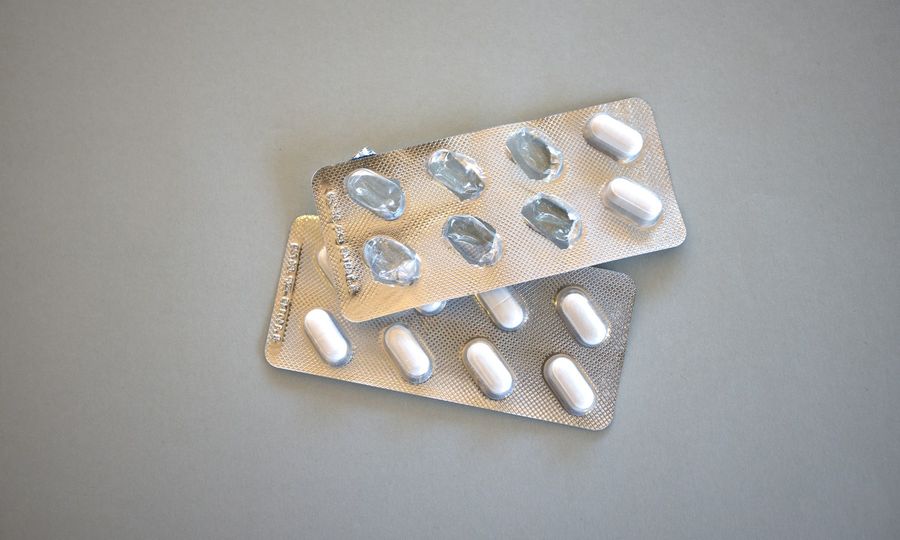 Two silver blister packs with white pills on a grey surface