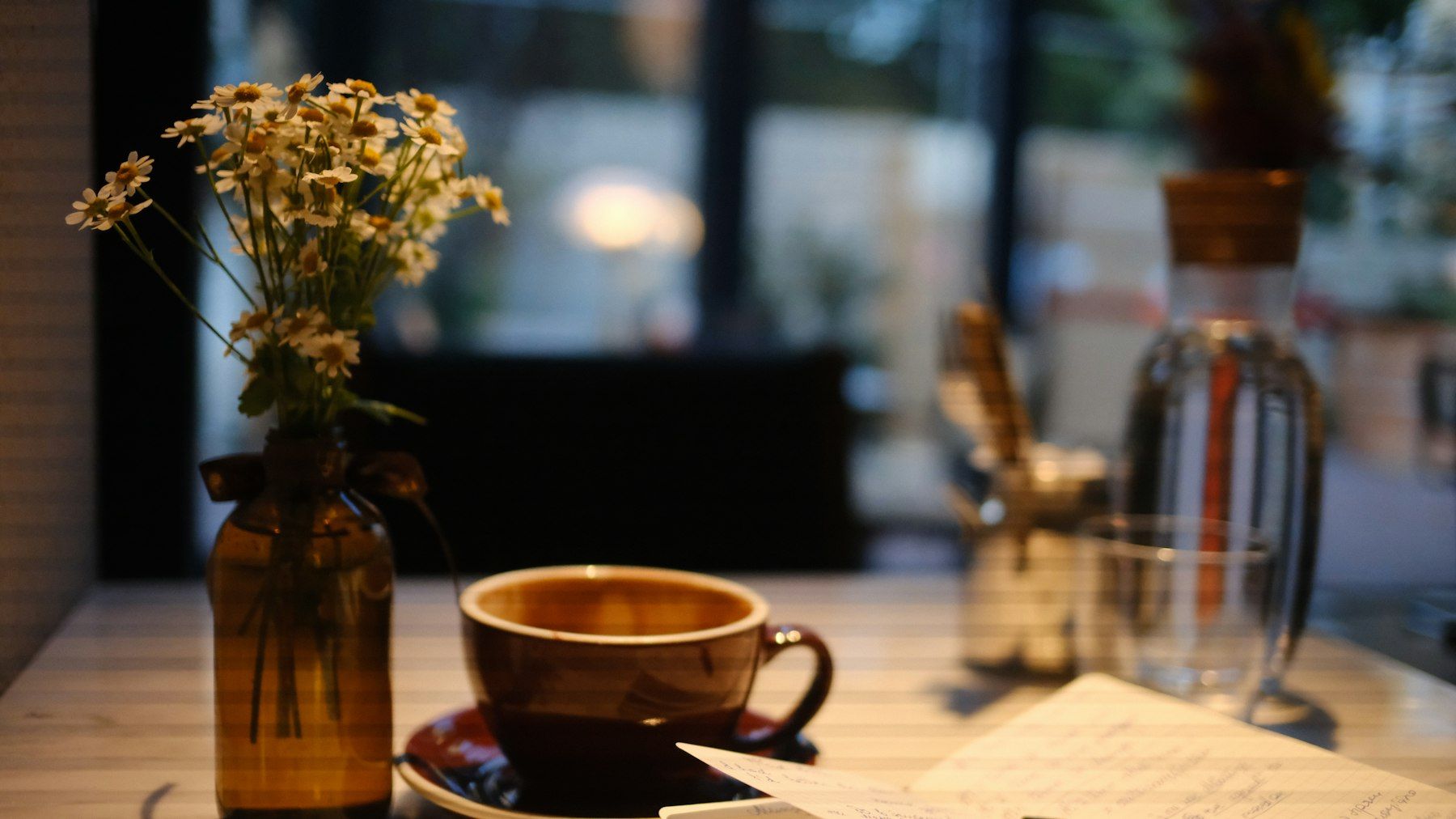 A cup of coffee and a vase of daisies on a table