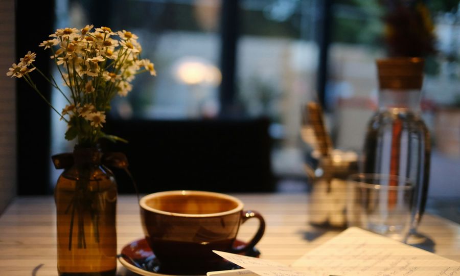 A cup of coffee and a vase of daisies on a table