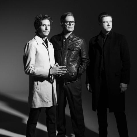The band Interpol photographed in a photography studio, lit dramatically, their shadows recede behind them.