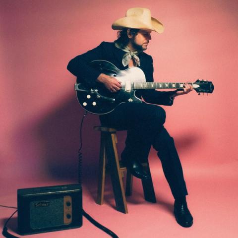 Musician Langhorne Slim posed with an electric guitar in a photography studio with a pink seamless backdrop