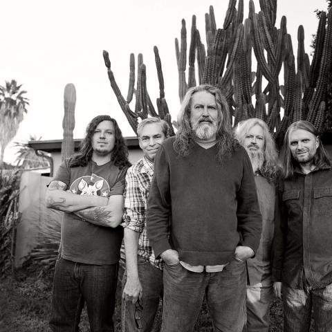 Musical group Meat Puppets photographed in black and white, behind them are a towering organ-pipe cactus, a saguaro and a palm tree