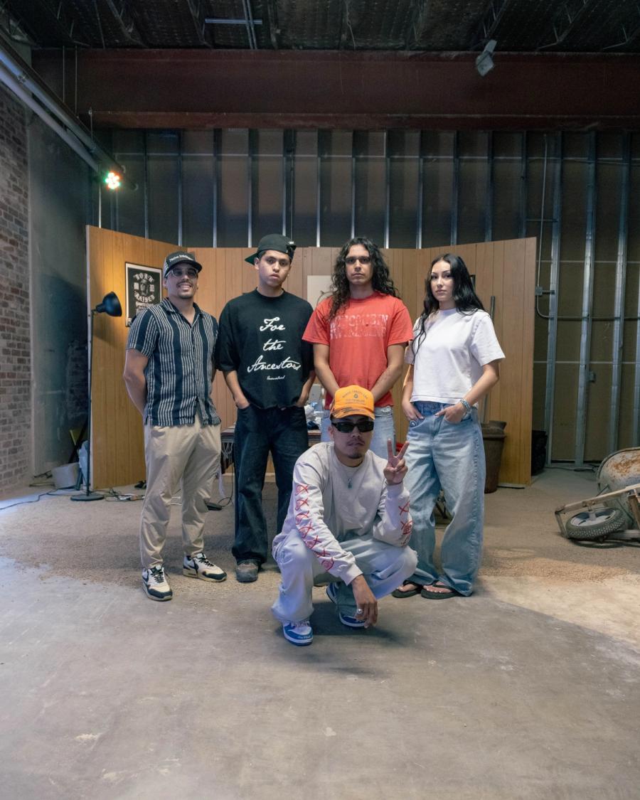 Group portrait inside a gallery or warehouse space with unfinished walls and concrete floor.