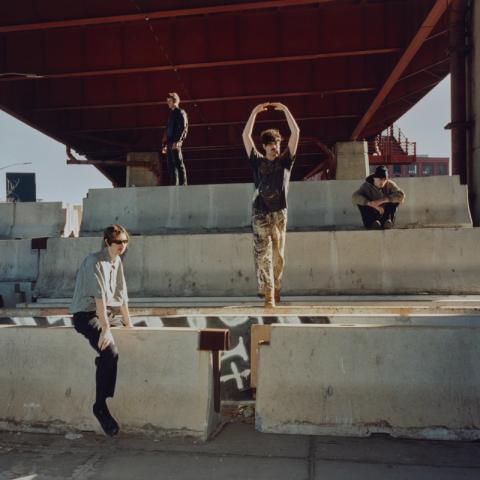 Music group Model/Actriz standing in an underpass type area on concrete barriers.